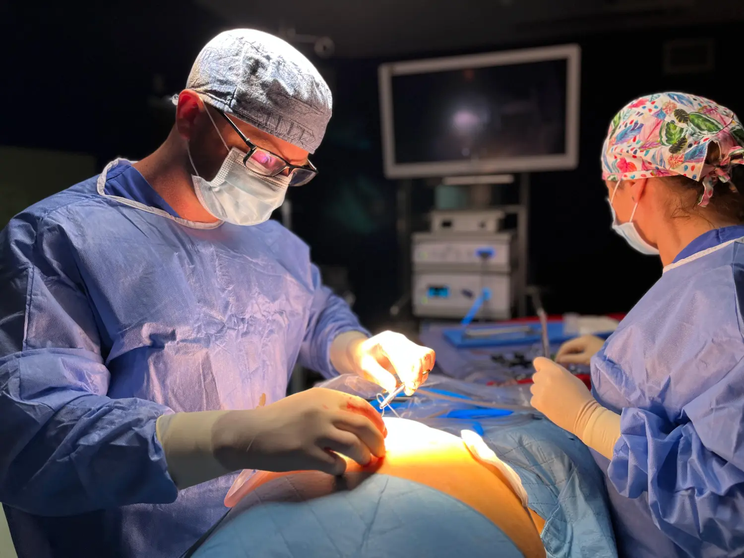 Dwóch chirurgów w fartuchach wykonuje zabieg w jasnym świetle chirurgicznym na sali operacyjnej.