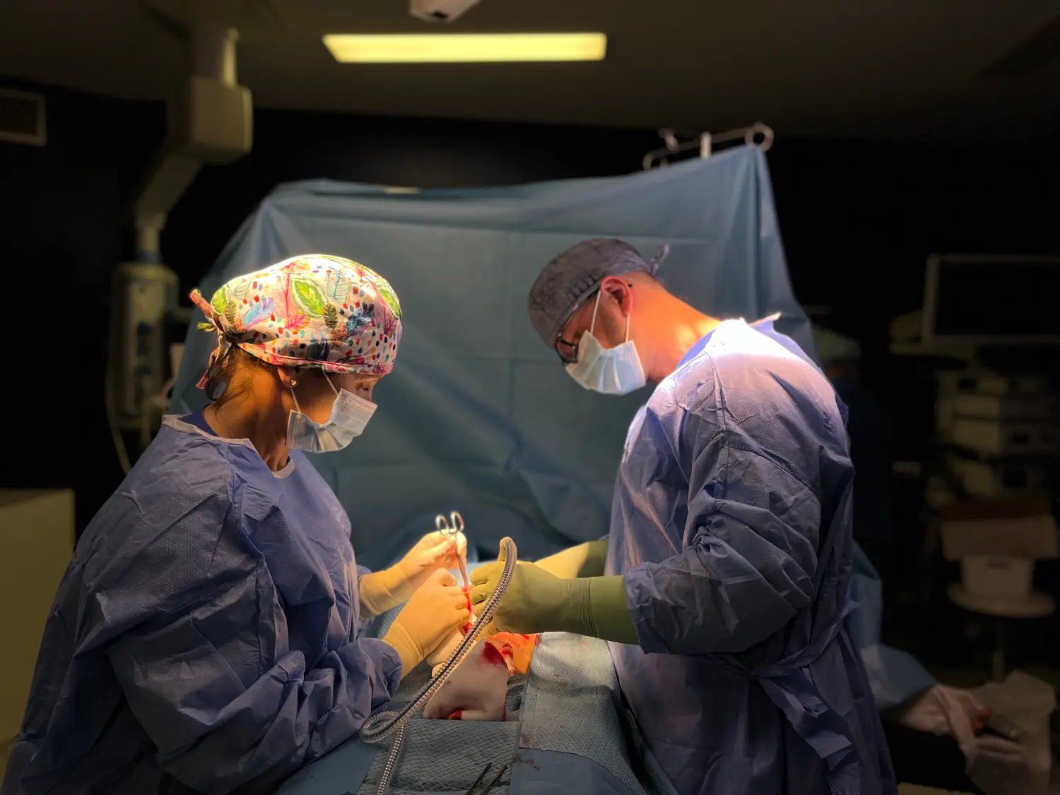 Dwóch chirurgów w fartuchach i maskach przeprowadza operację w jasno oświetlonej sali operacyjnej.