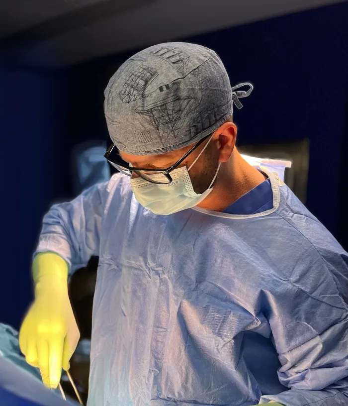 Chirurg w niebieskim fartuchu, masce i rękawiczkach skupia się podczas wykonywania zabiegu na sali operacyjnej.