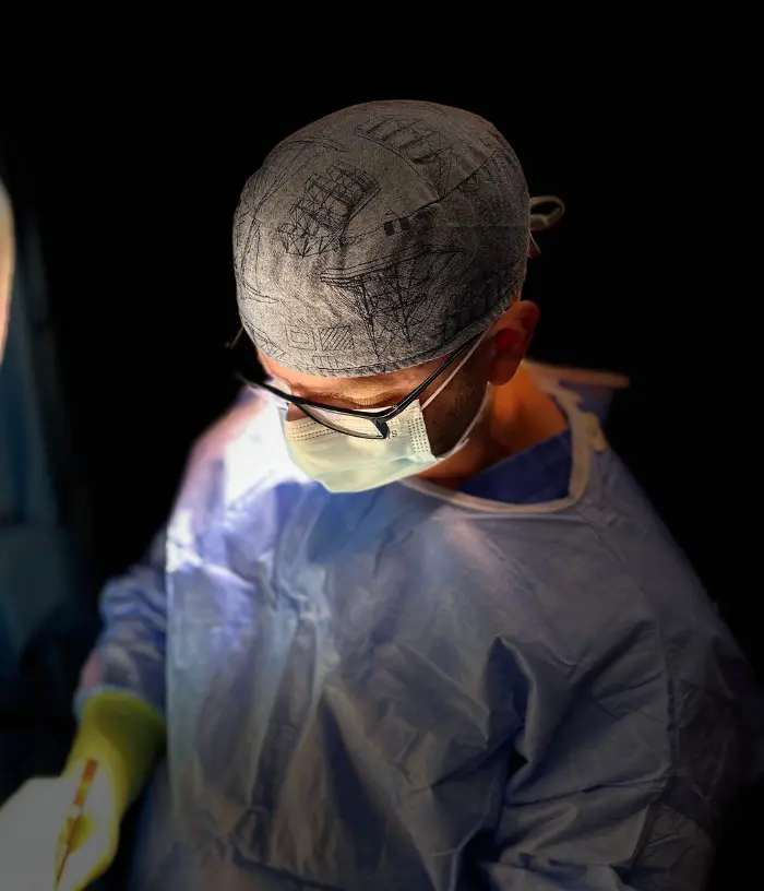 Chirurg w fartuchu, masce i rękawiczkach pracuje w jasnym świetle na sali operacyjnej.
